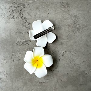 2 hair clips with frangipani flowers on a gray table